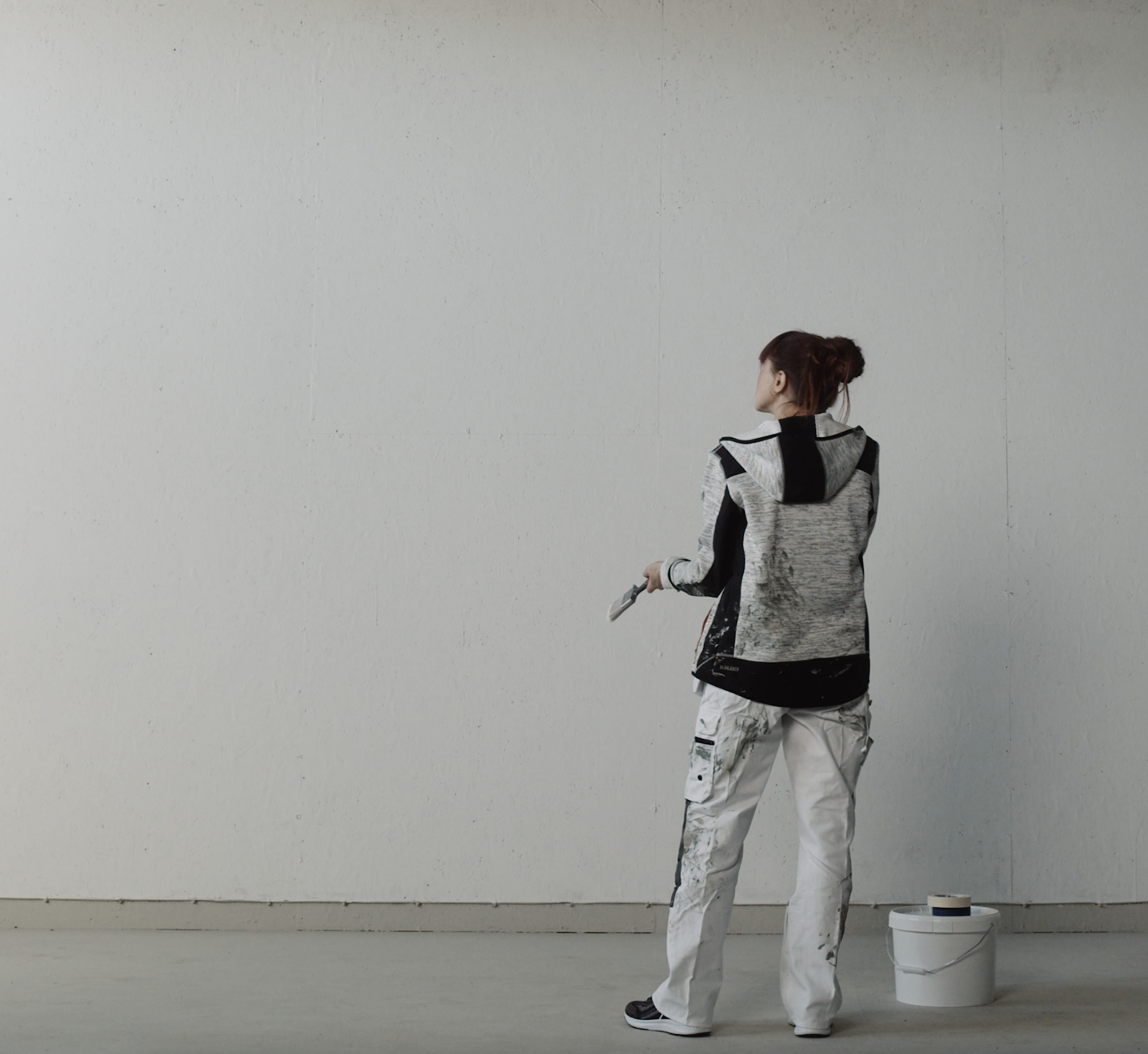 Målare framför stor vit vägg som håller liten pensel.