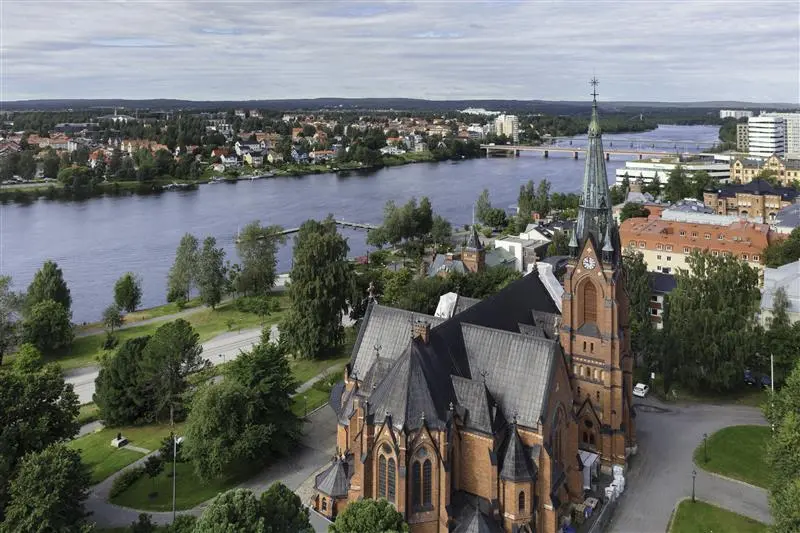 Flygbild över Umeå Domkyrka med Umeälven och stadens sommarlandskap i bakgrunden.