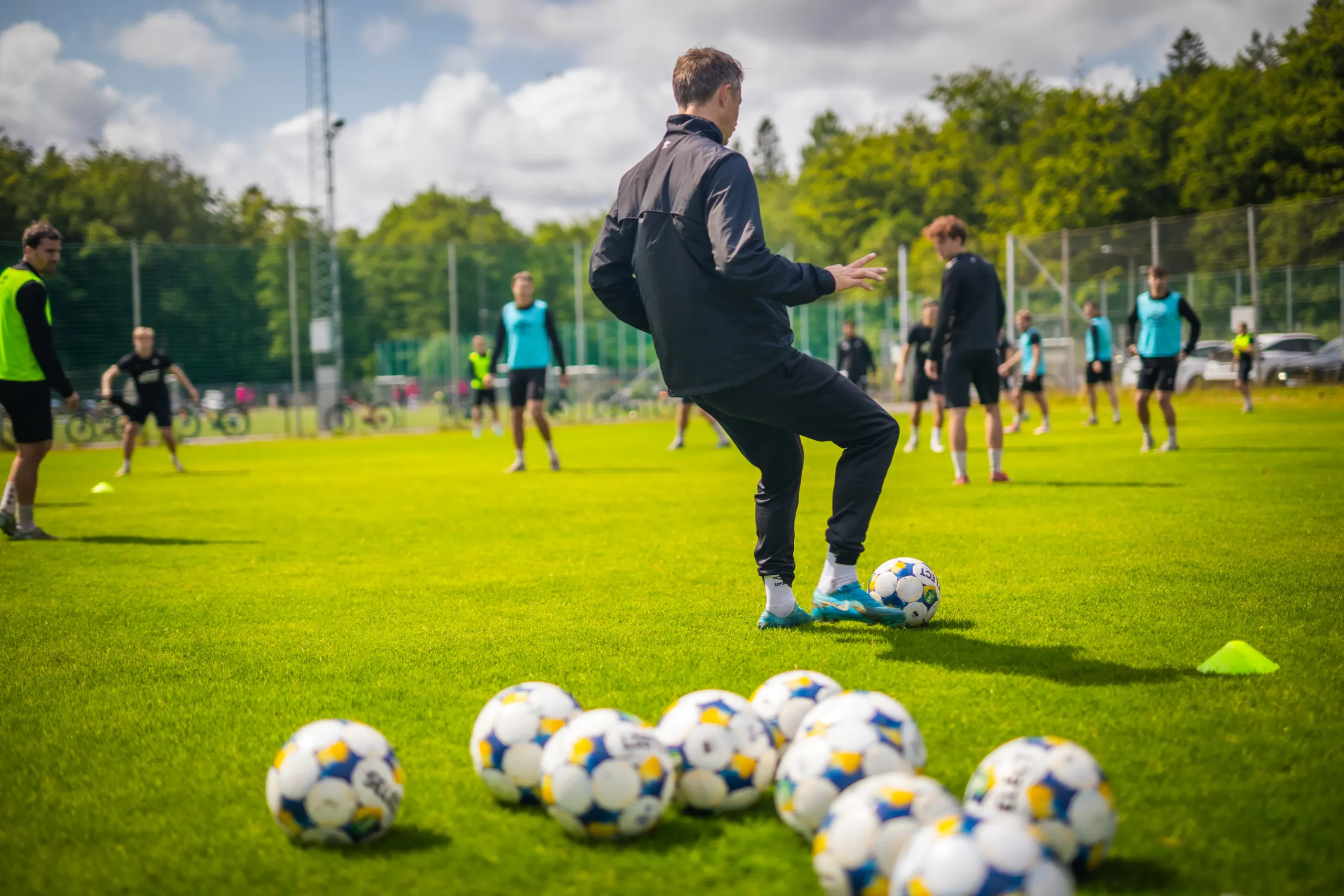 Spelare under en fotbollsträning med många bollar på planen.