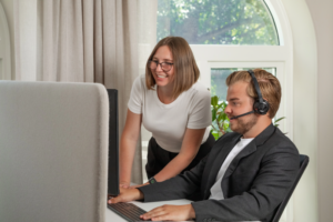 Två medarbetare på Factoringgruppen samarbetar framför datorn, en med headset och en som lutar sig fram och ler.